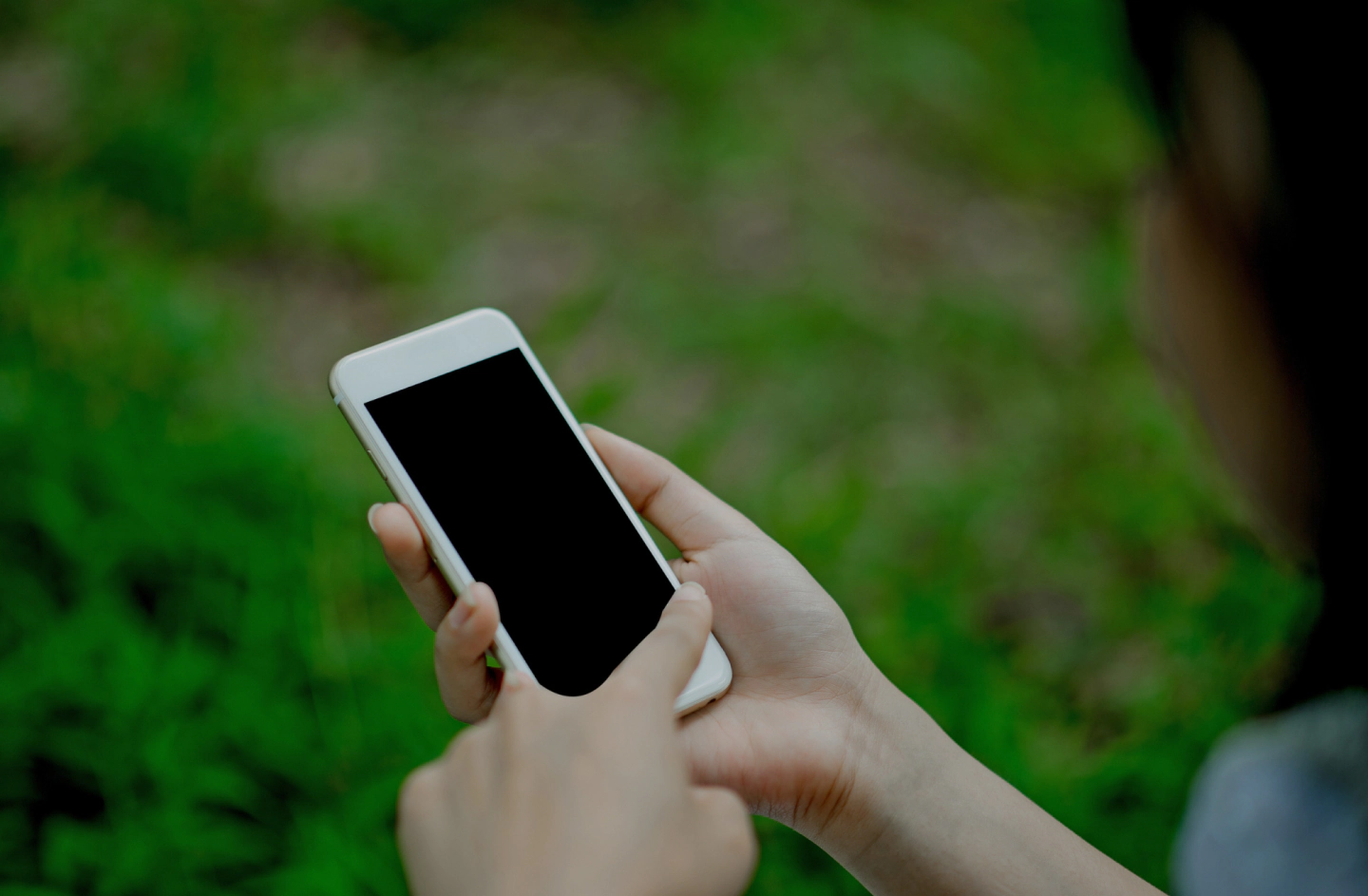 person holding a white cellphone with the hands and grass around