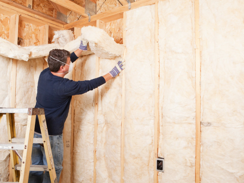 worker adding white fiber glass insulation on wood walls